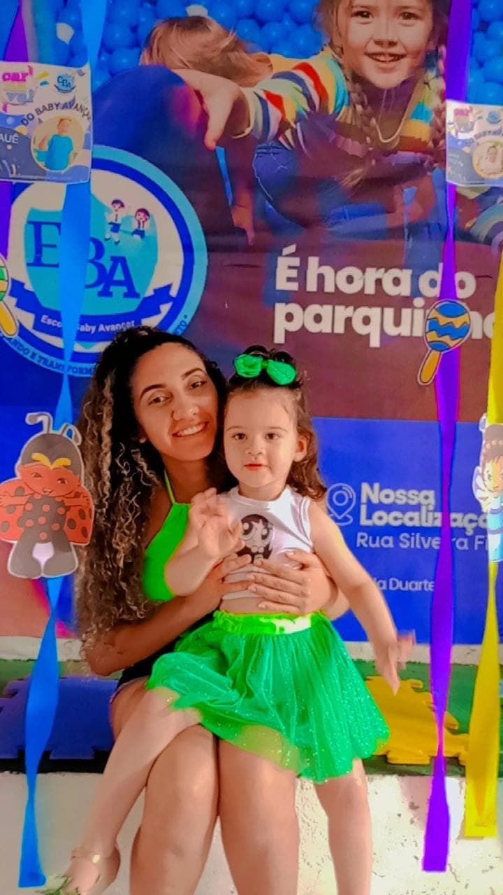 Educadora e aluna sorrindo abraçadas em frente ao painel do evento “É hora do parquinho”