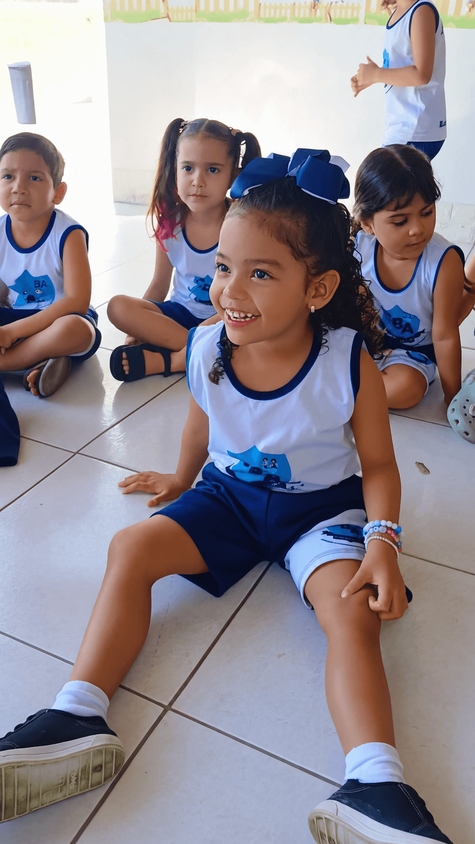 Grupo de crianças sorrindo durante atividade na escola, sentadas no chão da varanda