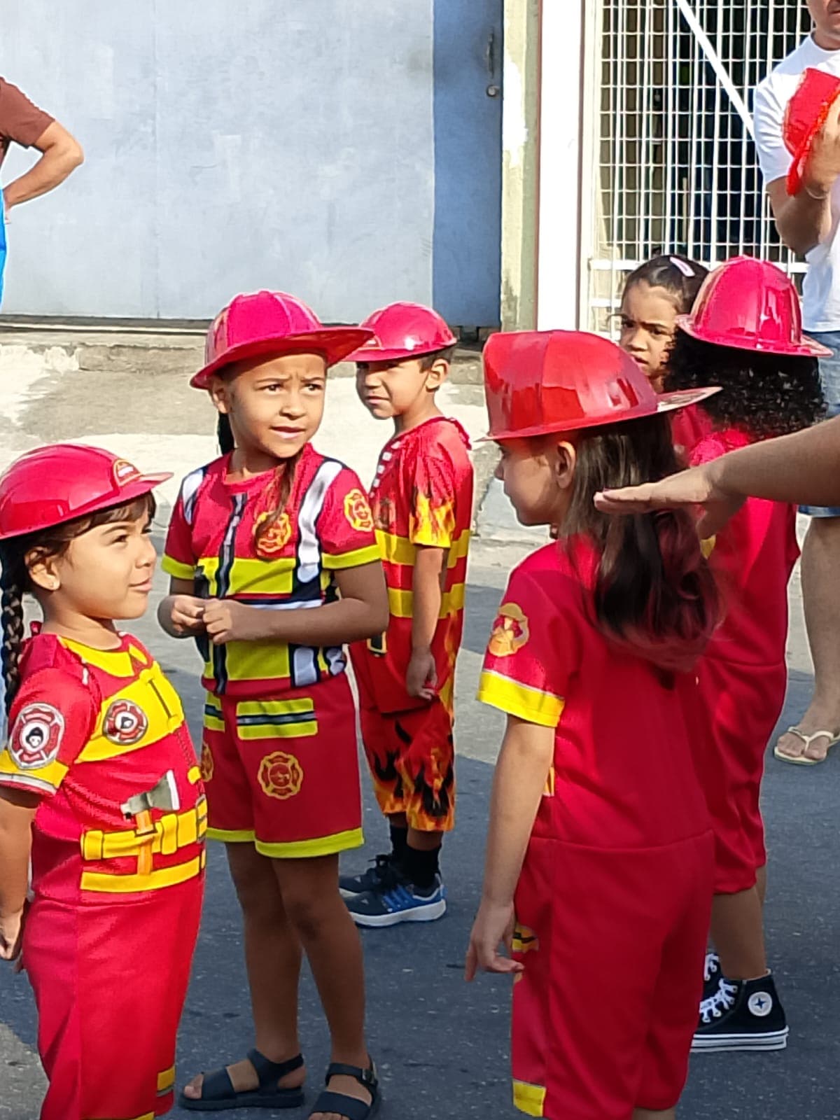 Crianças fantasiadas de bombeiro mirim, com capacete vermelho, em desfile do Colégio Baby Avançar