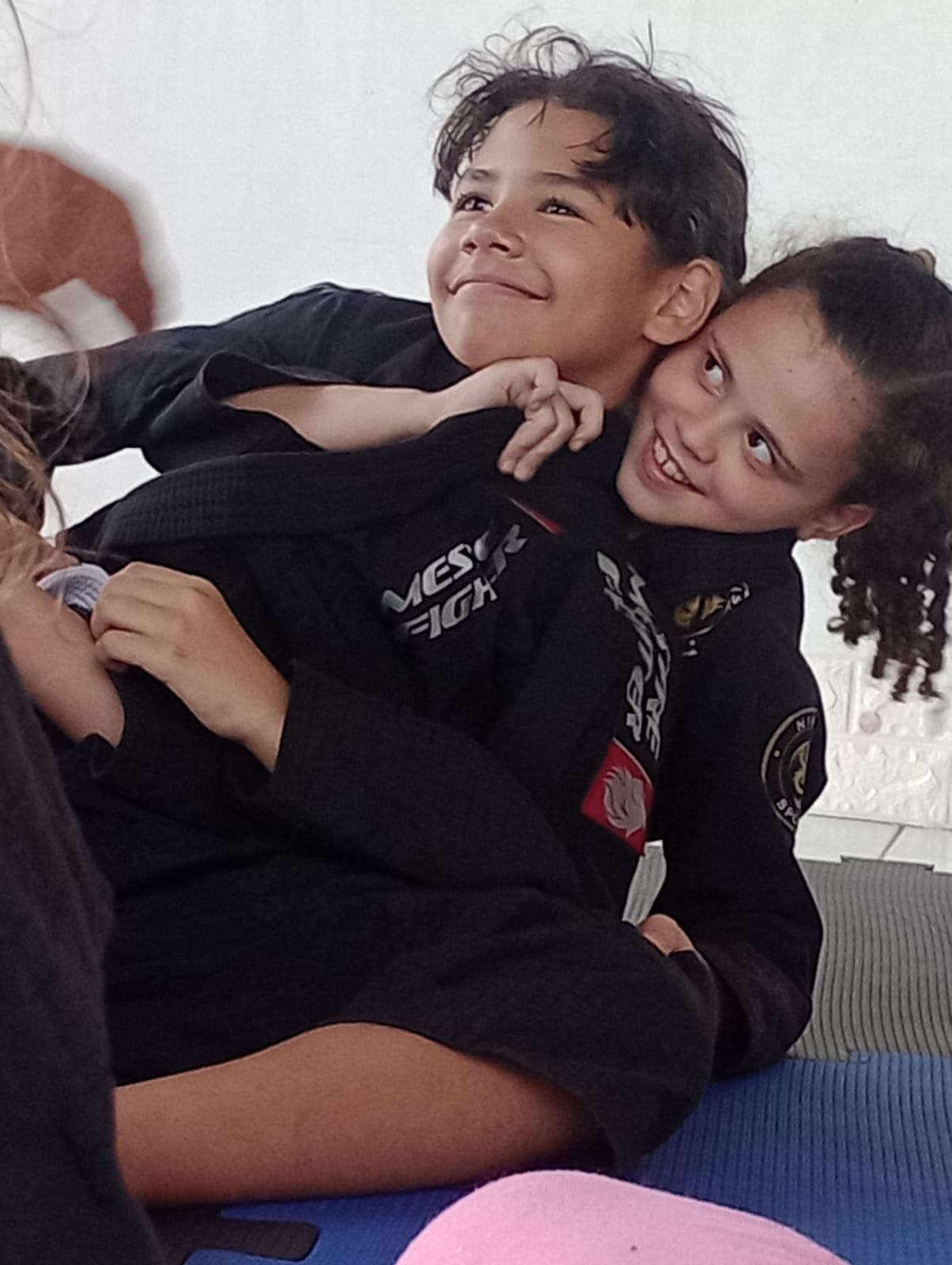 Duas crianças sorrindo durante aula de Jiu-Jitsu, vestindo kimono, em treino no Colégio Baby Avançar
