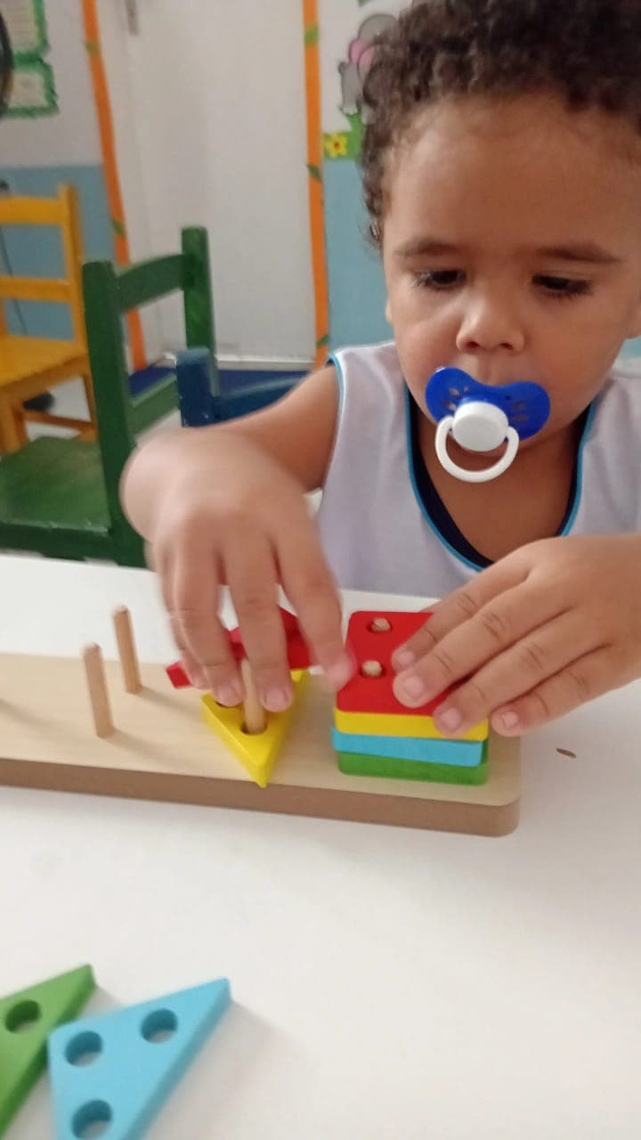 Criança pequena concentrada encaixando peças de madeira coloridas em brinquedo pedagógico na Educação Infantil